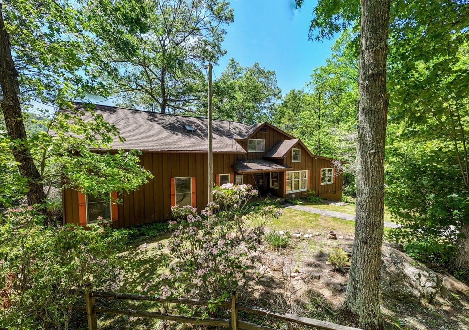 Side profile of the rustic brown cabin showcasing the multi-level deck and lush green forest surroundings.