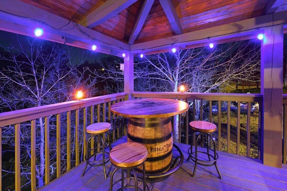 Rustic covered balcony with barrel table and stools illuminated by string lights for a cozy evening.
