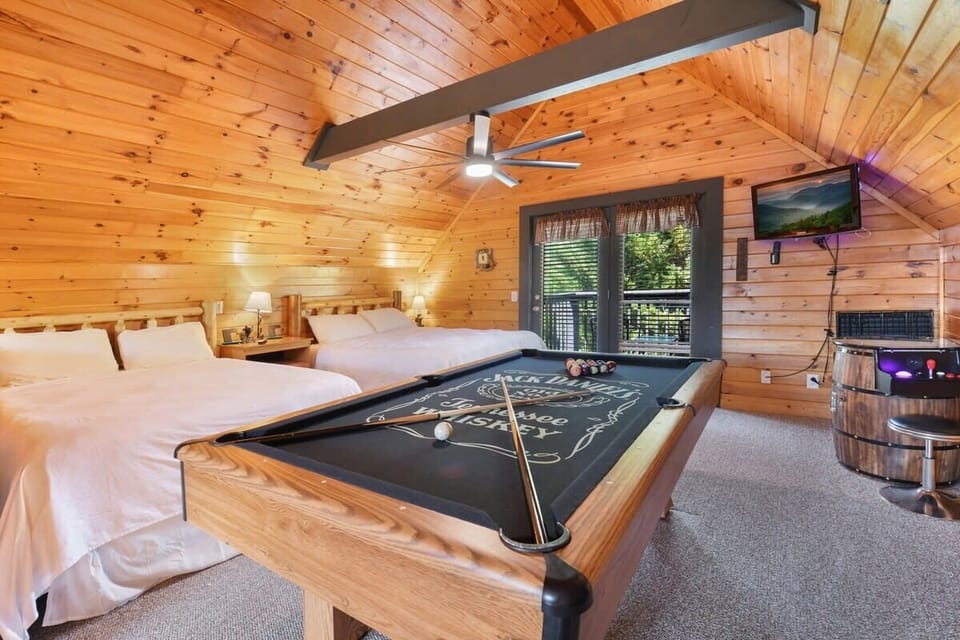 Rustic bedroom featuring two beds and a pool table with a scenic balcony view.