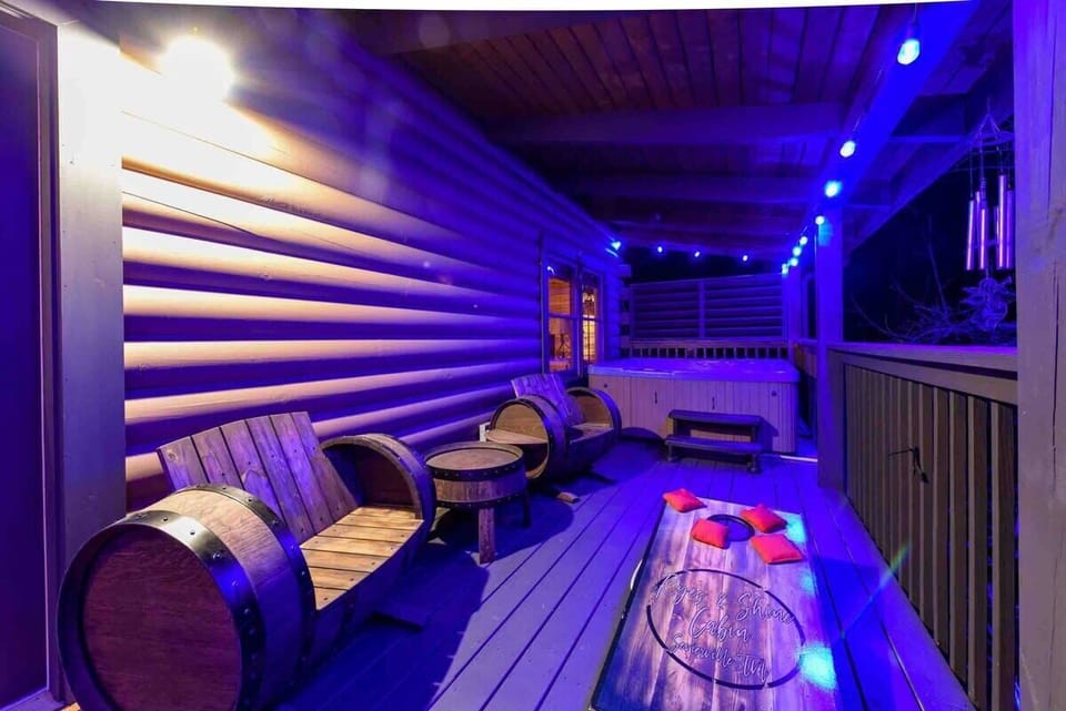 Relax on the rustic porch with barrel-style seating and a hot tub under ambient blue lighting.
