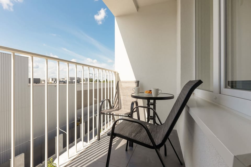 A balcony with a small table and two chairs, offering a relaxing spot with an open view of the sky and surroundings.

