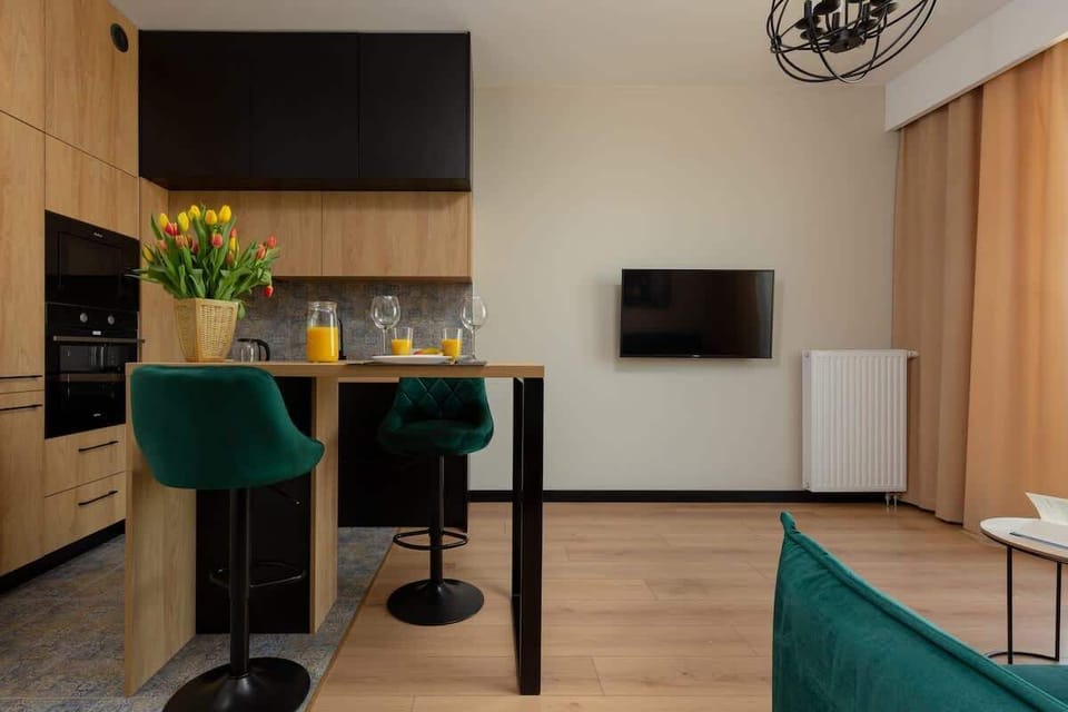 Another angle of the living room showcasing a dining area with a wooden table and green chairs, seamlessly blending with the open kitchen space.