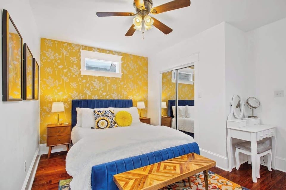 Bright and stylish bedroom featuring a bold accent wall, plush king bed, and thoughtful touches like a vanity and mirrored closet. A perfect blend of comfort and personality.