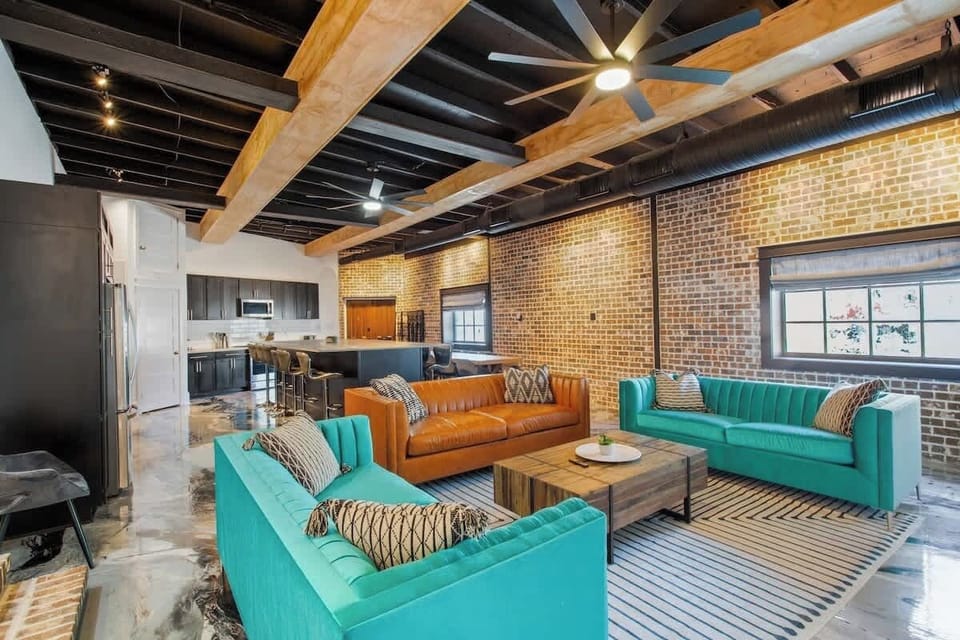 Spacious open living area with stylish seating, exposed brick, and high ceilings. Seamlessly connected to the kitchen, it’s perfect for relaxing, socializing, and enjoying time together in a vibrant setting.