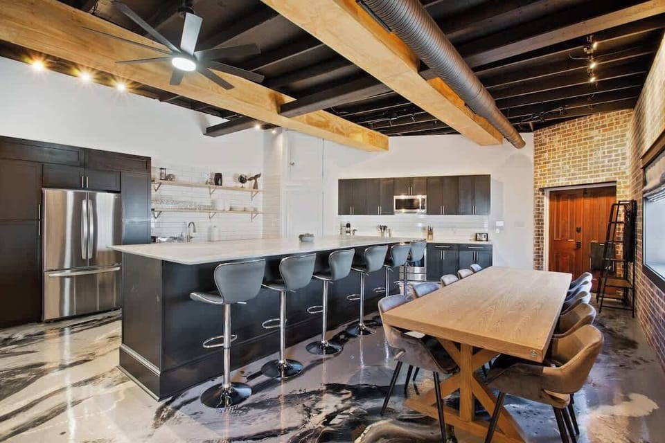 Modern chef’s kitchen with a large island, bar seating, and full dining table. High-end appliances, open shelving, and industrial-style details make it ideal for cooking, entertaining, and gathering together.