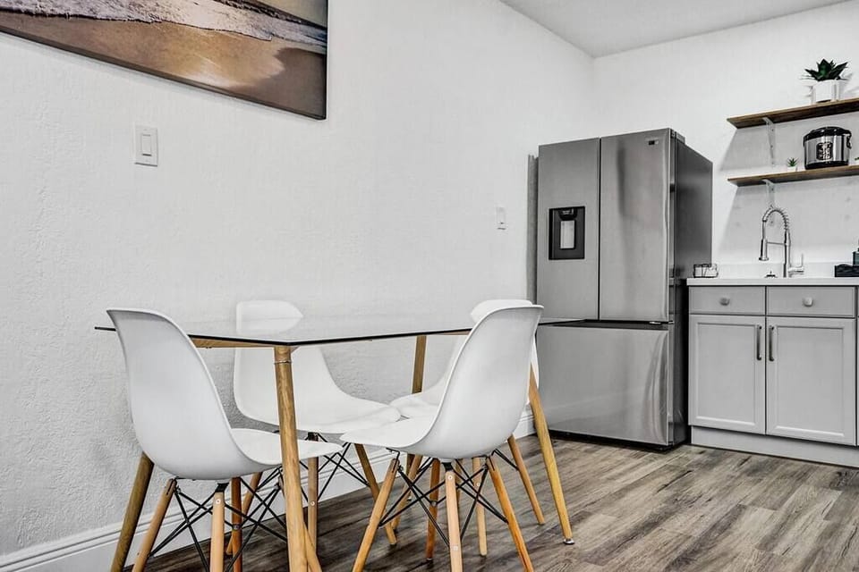 The table where you eat can fit 4 people. The pretty chairs match the modern style and are cozy to sit in. The big fridge is made by Samsung and has double doors. It can keep all the food you got from the store cold, so it stays fresh.