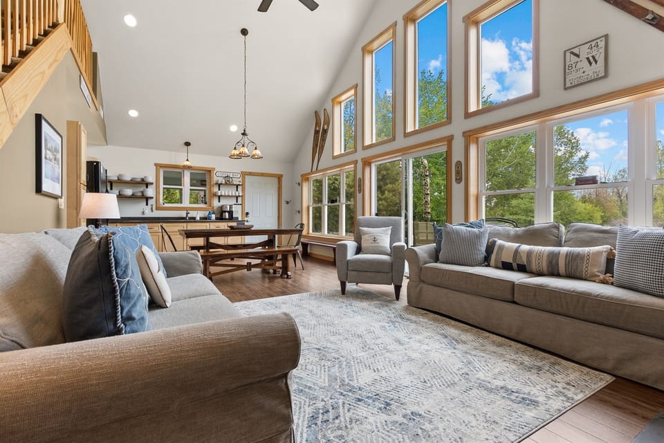 The whole main floor in a single look — living room, dining table, kitchen, Coffee Bar, and a wall of windows bringing Sawyer Harbor in from every angle. Ten guests, one space, zero compromise.
