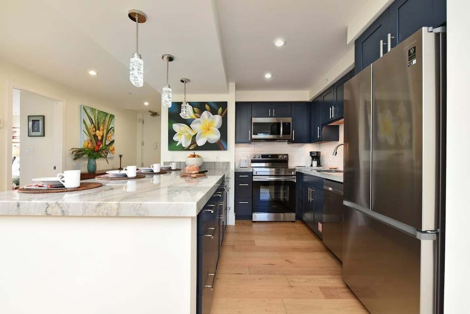 Contemporary kitchen with marble island, pendant lighting, stainless appliances, and dark cabinetry.