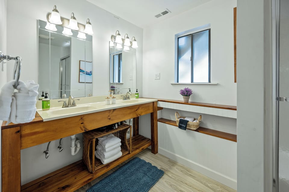 Spacious lower-level bathroom vanity with two sinks, large mirrors, and open storage.