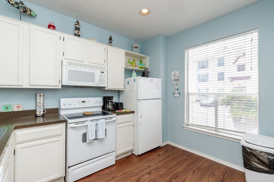 Your fully equipped kitchen features white appliances, ample storage, and peaceful views through large windows—perfect for preparing your favorite meals.