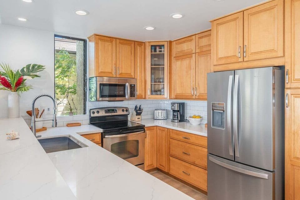 Modern kitchen with wooden cabinetry, stainless steel appliances, and a window framing tropical greenery