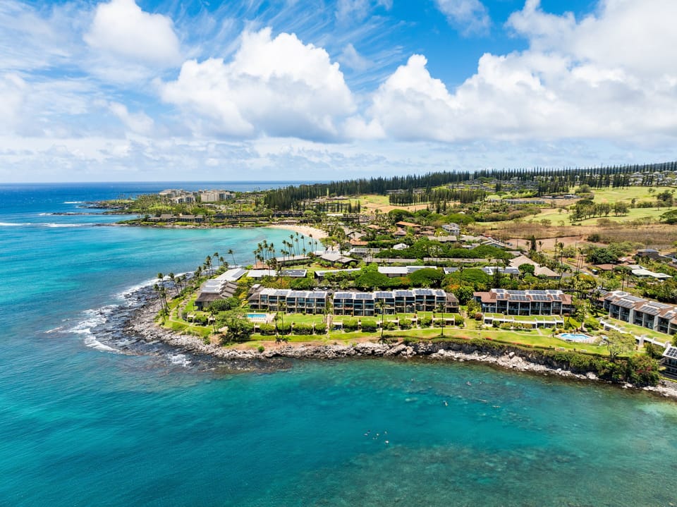 Aerial view of turquoise waters, rocky shoreline, and resort complex surrounded by lush greenery