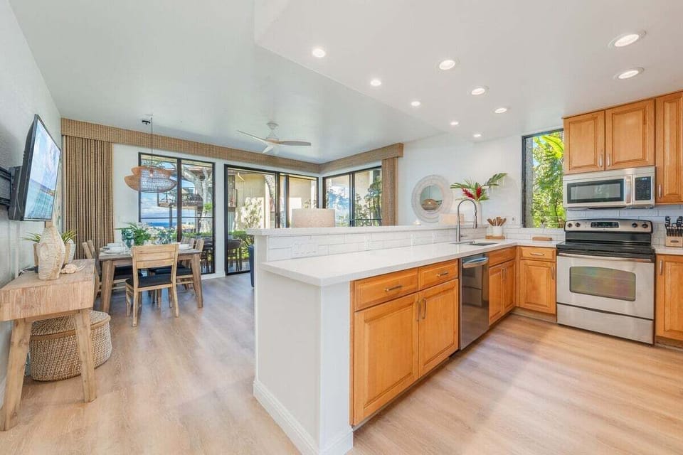 Bright kitchen with light wood cabinetry, stainless steel appliances, and white countertops opening to ocean views