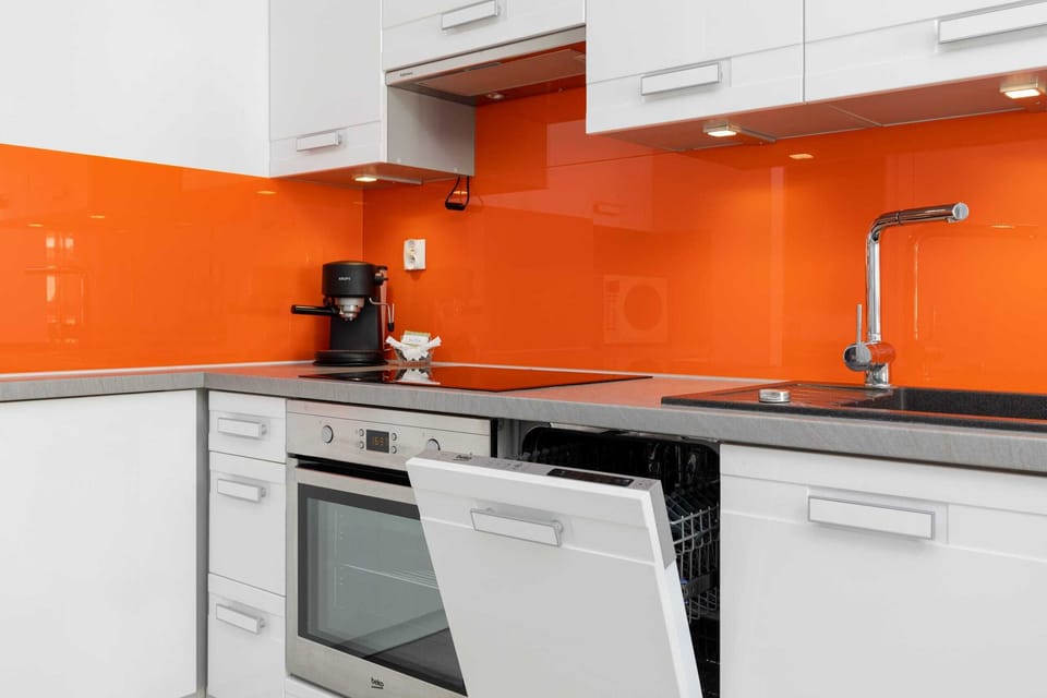 A close-up of the kitchen showing a bright orange backsplash, a kettle, coffee machine, and sink.
