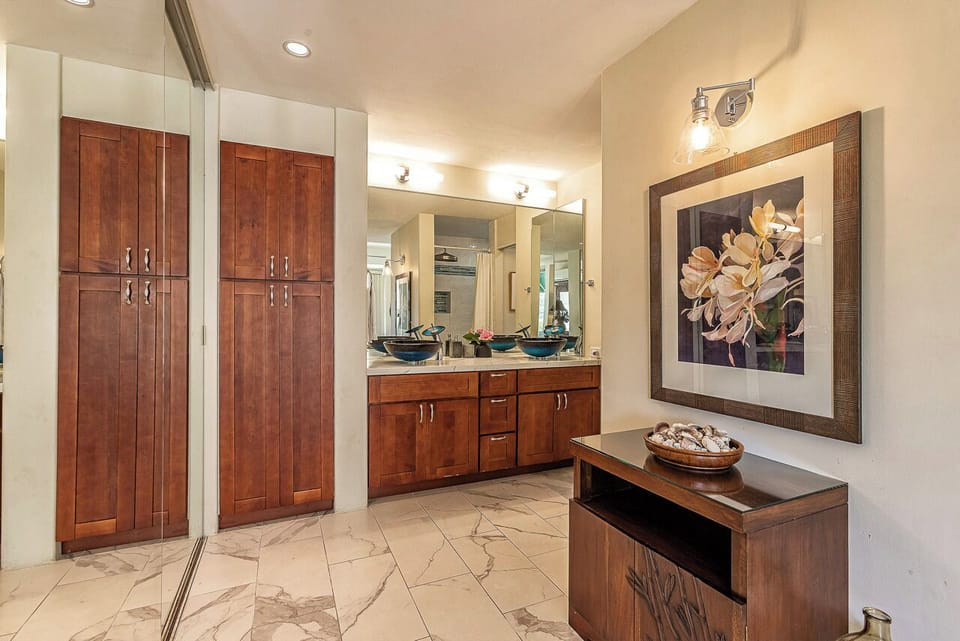 Your private bathroom sanctuary features elegant marble floors, custom wood cabinetry, dual vessel sinks, and art-adorned walls—a luxurious space designed for comfort and style.