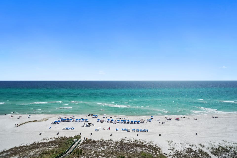 Pristine Gulf Coast beach with emerald waters and white sand stretches along the shoreline under brilliant blue skies.