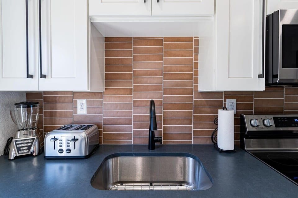 Modern kitchen sink area with stainless steel appliances and a warm brown tile backsplash