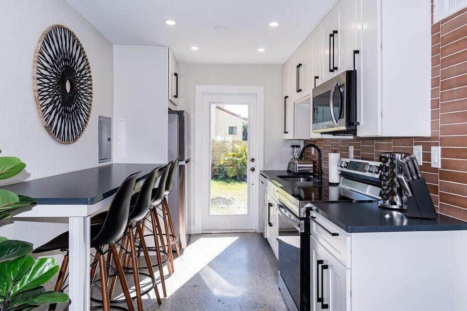 Modern kitchen with black countertops, white cabinetry, and a breakfast bar with seating for four.