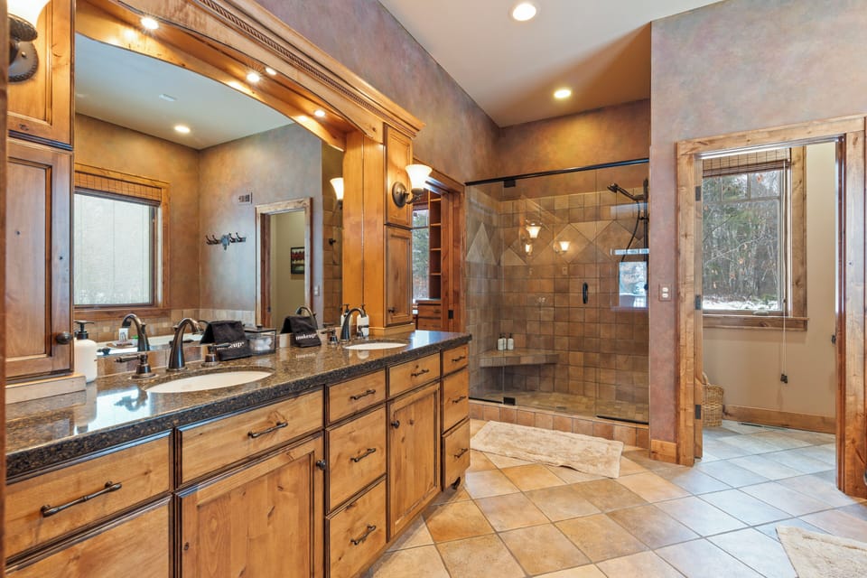 Indulge in your spacious master bathroom featuring dual vanities, a luxurious tiled shower, and elegant wood cabinetry for the ultimate relaxation.