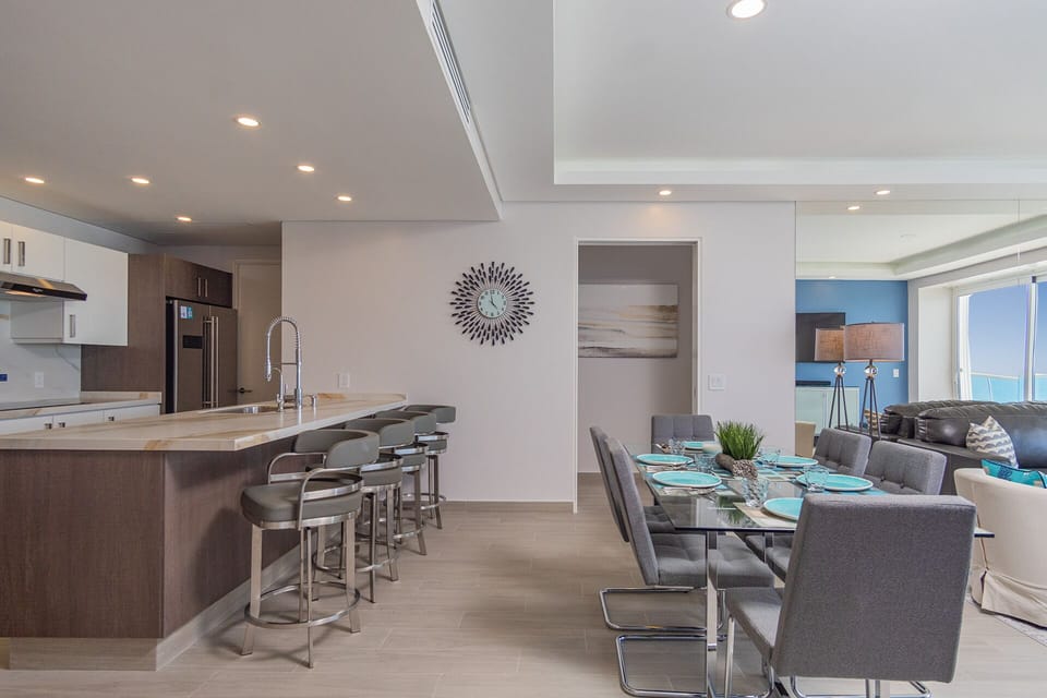The kitchen counter with bar stools and the dining table.