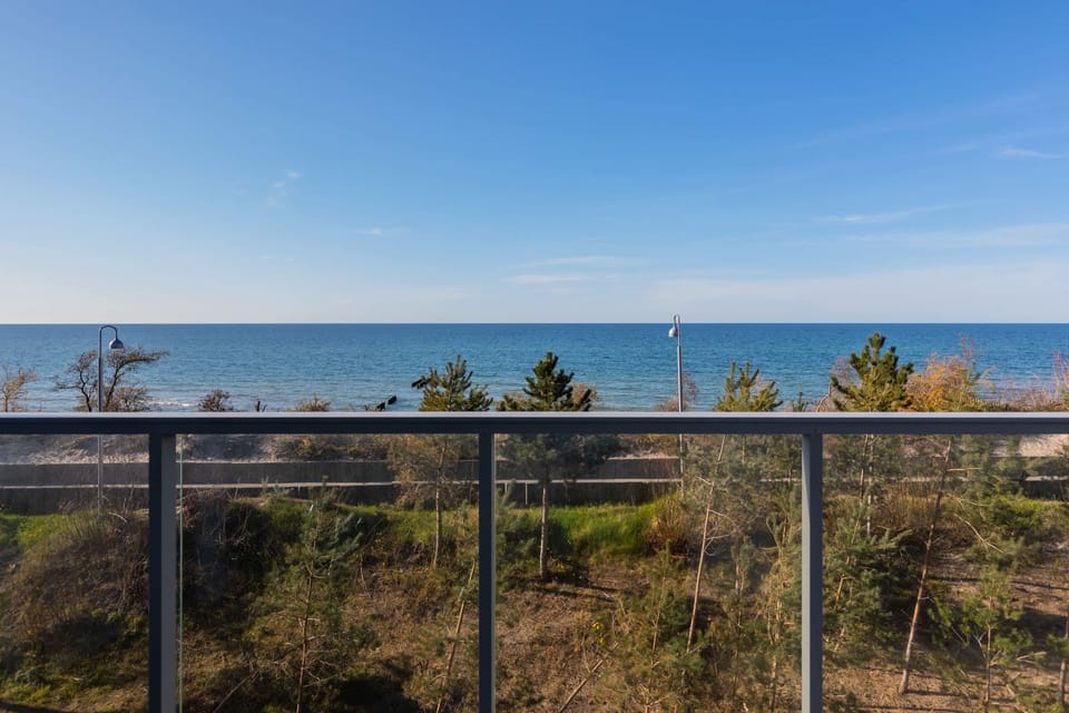 A balcony with a small outdoor table and chairs overlooks a beautiful sea view. Glass railings provide unobstructed vistas, creating a peaceful space to relax.