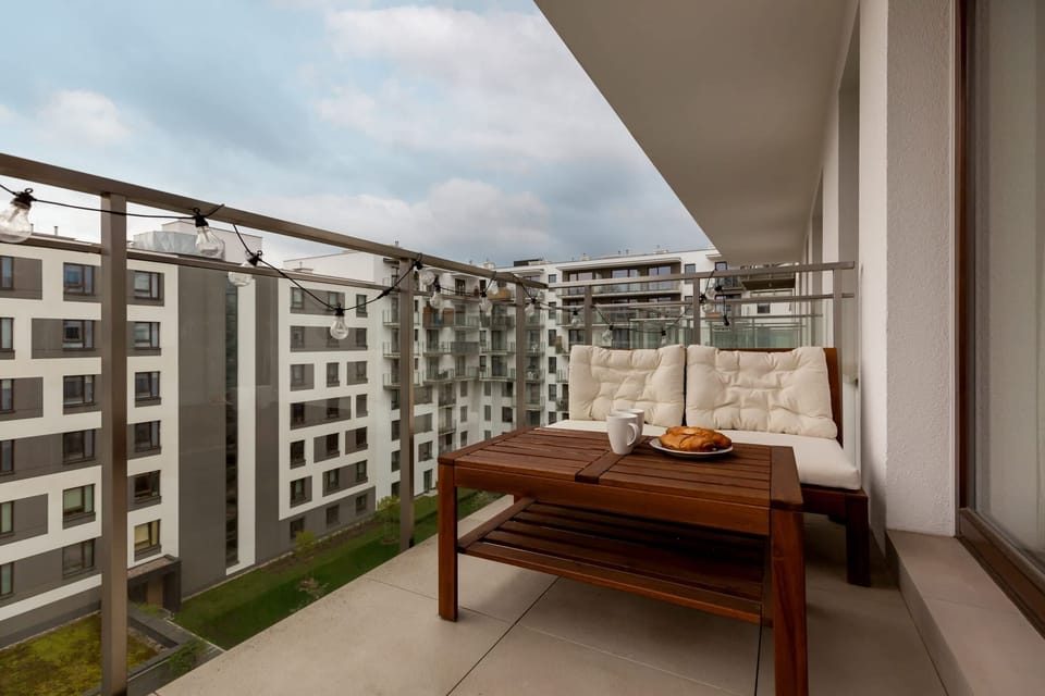  A balcony with outdoor seating and a view of the modern apartment buildings and courtyard.