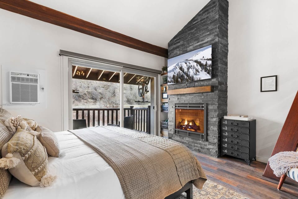 Wrap yourself in warmth beside the fireplace while gazing at snowy mountain views through your private balcony doors—your cozy retreat awaits.