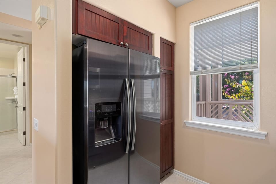 - Stainless steel side by side refrigerator with water and ice dispenser   - Set between tall wood cabinets for a built in, seamless appearance   - Nearby window brings in natural light to brighten the kitchen area