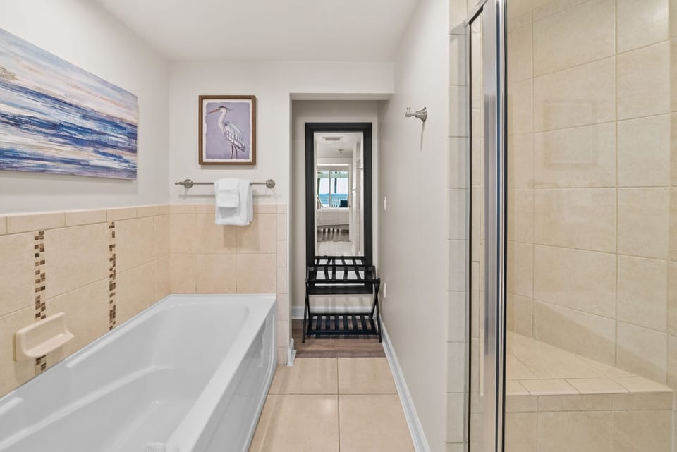 Unwind in your spacious bathroom featuring both a soaking tub and separate glass shower, with coastal artwork and fresh towels waiting.