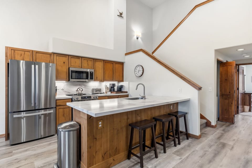 Your full kitchen features stainless steel appliances, warm wood cabinetry, and a bright island with seating—perfect for gathering over morning coffee or prepping meals together.