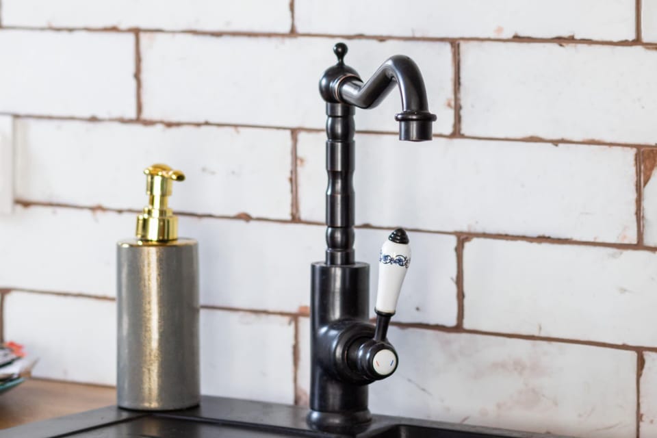 A close-up of a black kitchen faucet mounted against white brick-patterned tiles, adding a rustic touch.