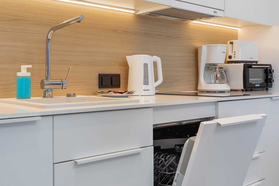 A kitchen with white cabinets and wooden accents, equipped with essential appliances and a sleek design.