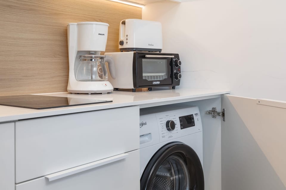 A combination of a kitchen and laundry area featuring a washing machine, a microwave, and cabinets for storage.