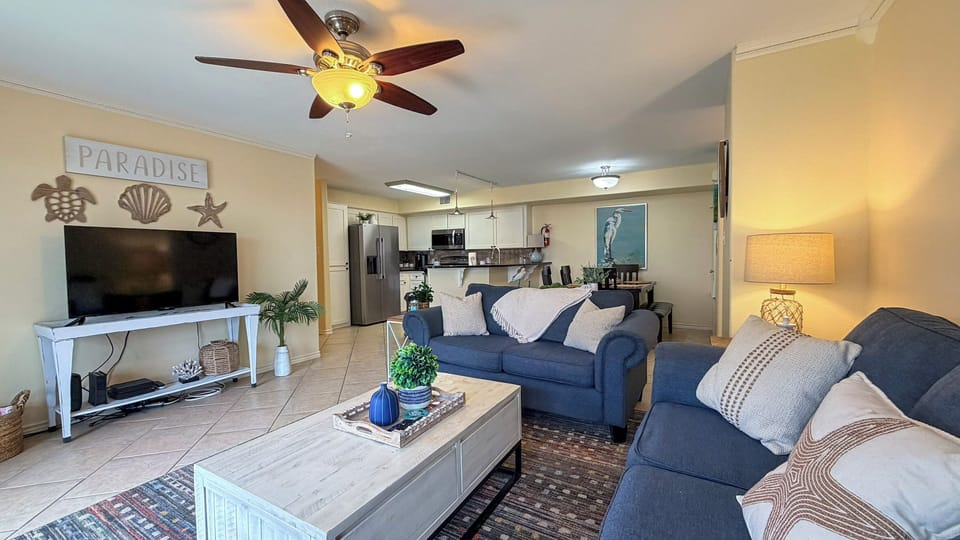 Your spacious living area features comfortable blue sofas, ceiling fan, and open kitchen—perfect for relaxing after beach days.