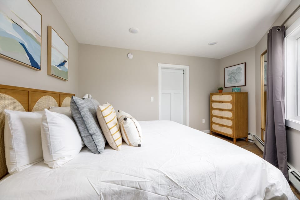 Peaceful bedroom retreat w/ layered pillows, warm wood accents & dresser for extended stays.