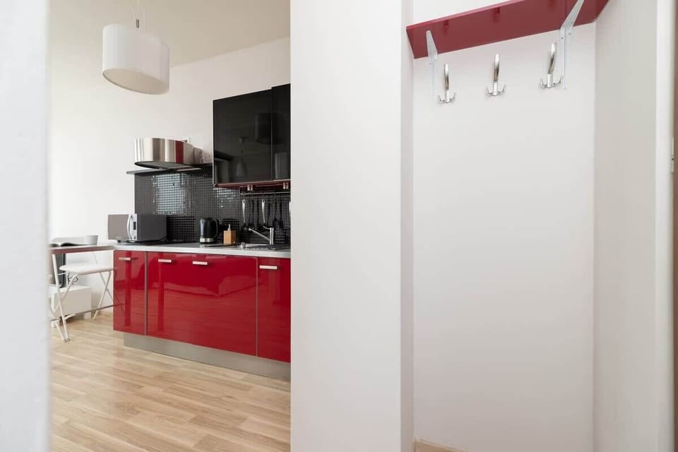 A modern kitchen with vibrant red cabinets, a dining table with white chairs, and wooden flooring.