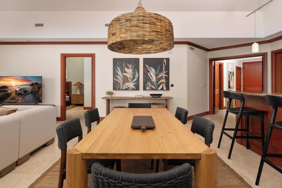Picture yourself gathering around this stunning wood table, where a handcrafted woven pendant casts a warm glow over your meals and conversations. The open layout flows seamlessly into cozy spaces beyond.