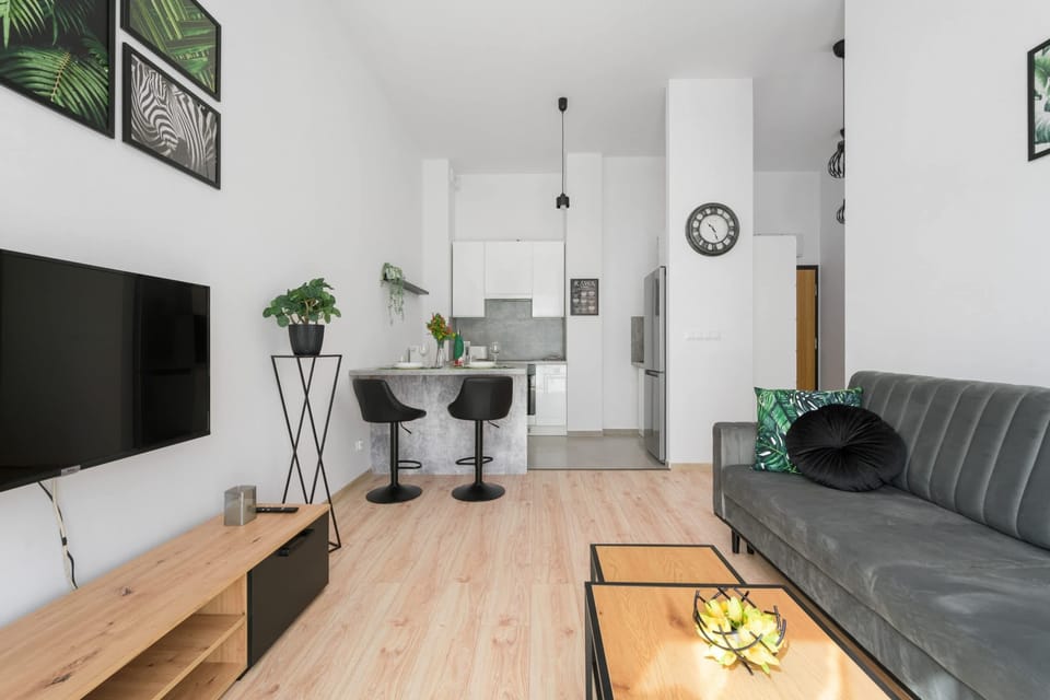 A modern living room featuring stylish furniture, including a dark sofa and a wooden TV stand. The large windows provide plenty of natural light.