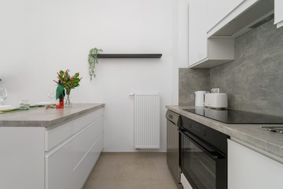 A minimalist white kitchen with cabinets, a built-in stove, and a countertop. A plant and vase add a touch of color.