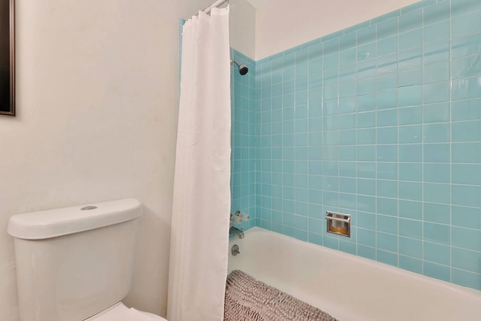 Bright, retro bath with aqua tile, shower/tub combo, and plush mat.