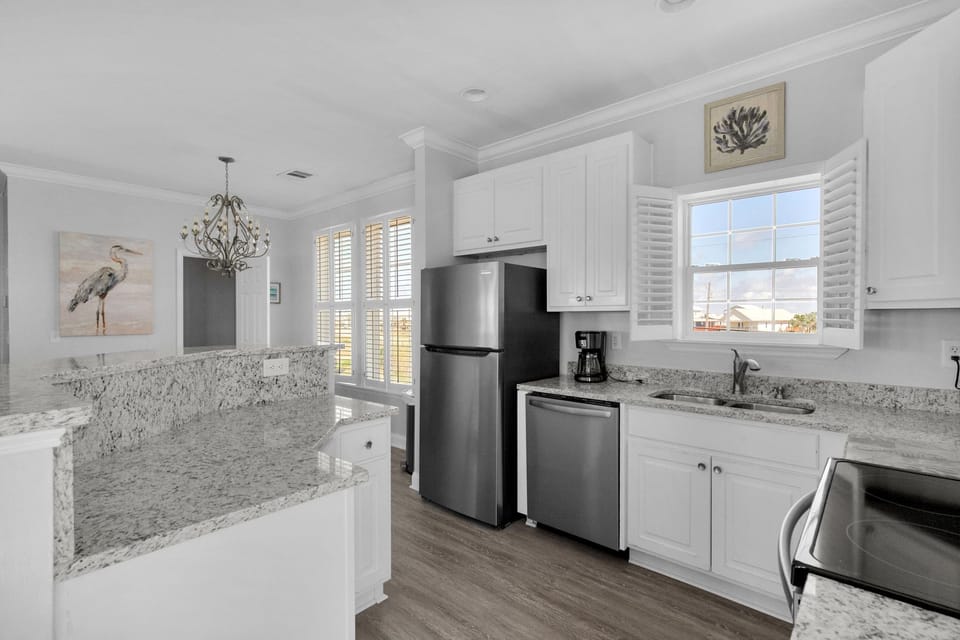 Your gourmet kitchen features granite counters, stainless appliances, and coastal charm with elegant chandelier lighting for memorable meal preparation.