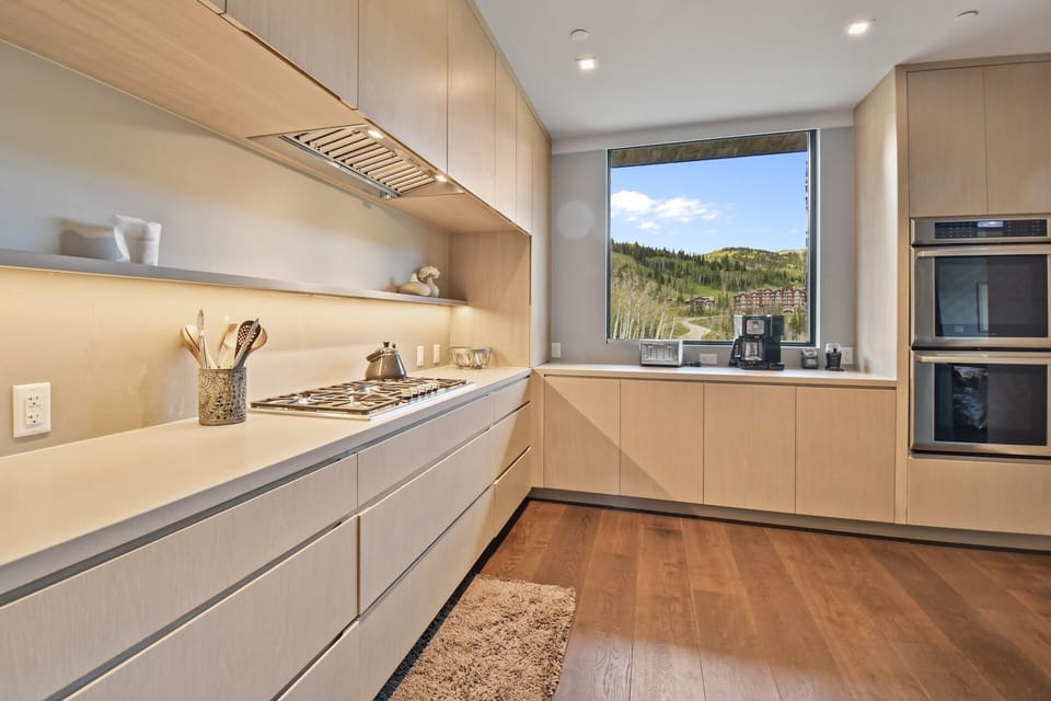 Your fully equipped kitchen features modern appliances and warm wood tones, with stunning mountain views framing your culinary space and morning coffee moments.