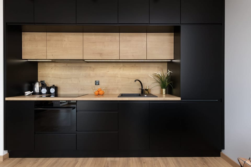 A sleek and minimalist kitchen with black cabinetry and wooden accents. The design includes modern appliances and subtle greenery for a touch of freshness.