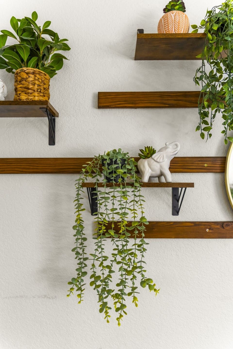 Thoughtful Wall Decor: Enjoy small, charming touches throughout the home with floating wooden wall shelves adorned with cascading faux greenery, decorative accents, and warm wooden paneling details.