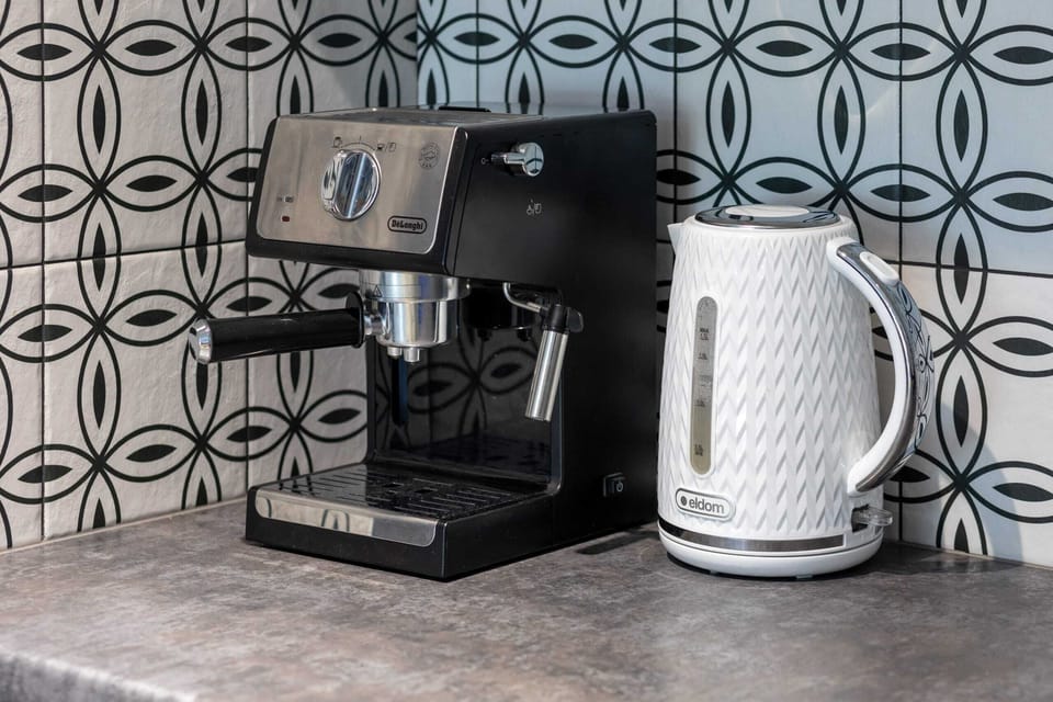 A close-up of a coffee station in the kitchen, featuring a black coffee machine, white kettle, and patterned backsplash.