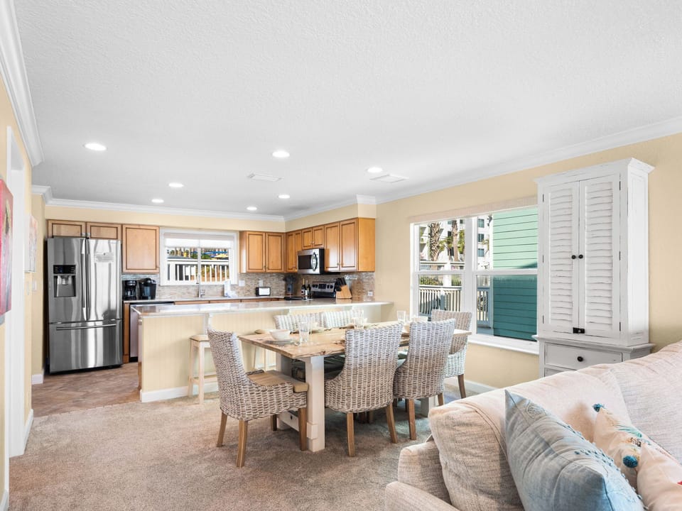 The spacious open-plan living area seamlessly blends kitchen, dining, and lounge spaces with coastal-inspired furnishings and abundant natural light.