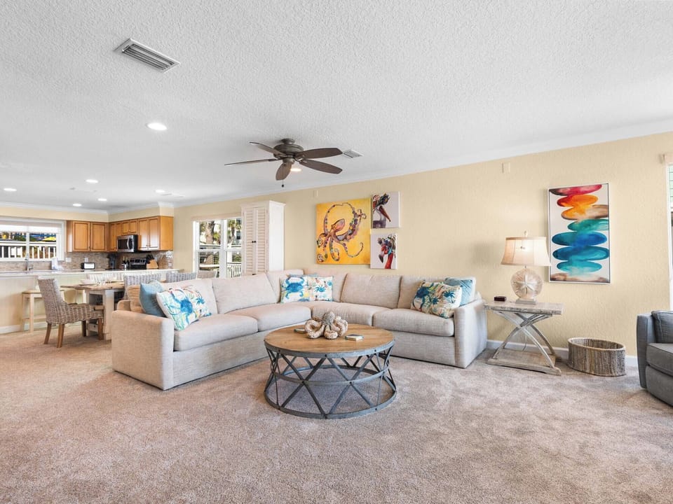 Unwind in the living area with plush sectional seating, vibrant coastal art, and an open-concept flow to the fully equipped kitchen.