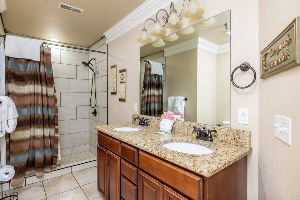 A spacious full bath featuring double sinks, a sleek stand-up shower, and a pristine toilet, all stocked with fresh, plush towels and starter essentials toiletries. 