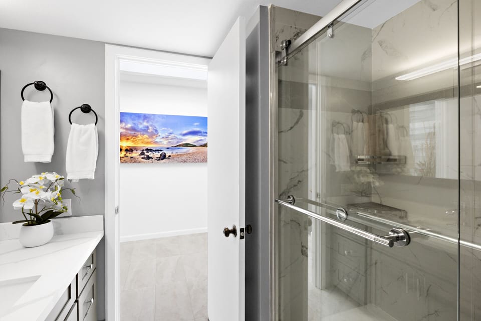 Enjoy a refreshing shower in this modern bathroom featuring stylish decor, sleek countertops, and beach-inspired artwork that enhances the coastal ambiance.