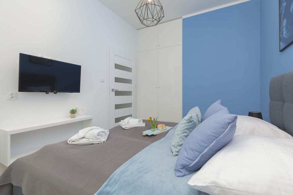 A cozy bed adorned with crisp white linens and subtle gray accents, bathed in soft natural light streaming through the window. The design is simple yet sophisticated, creating a tranquil and inviting atmosphere.